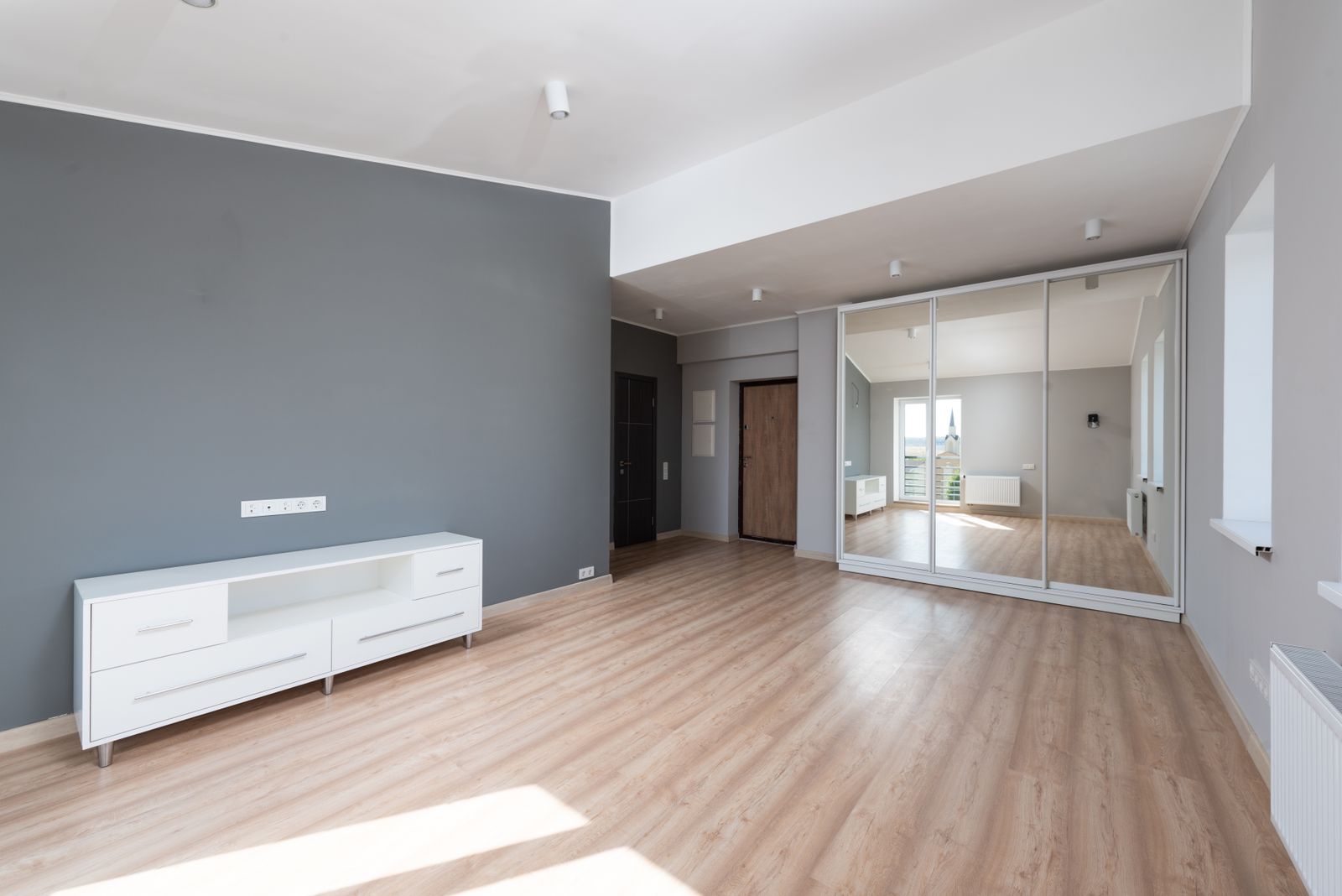 Spacious empty room with wooden flooring and minimalist style furniture.